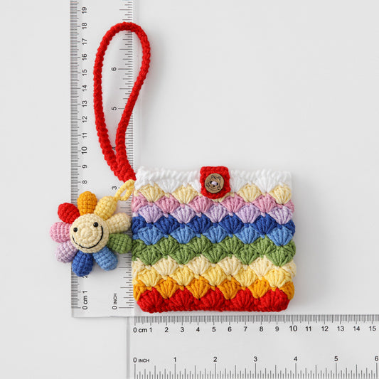 Colorful crocheted pouch with a bee charm next to a ruler for scale on a white background
